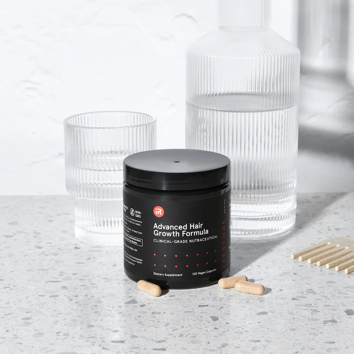 Image of the Advanced Hair Growth Formula placed on a table with tablets around it. A glass and jar of water are also behind it.